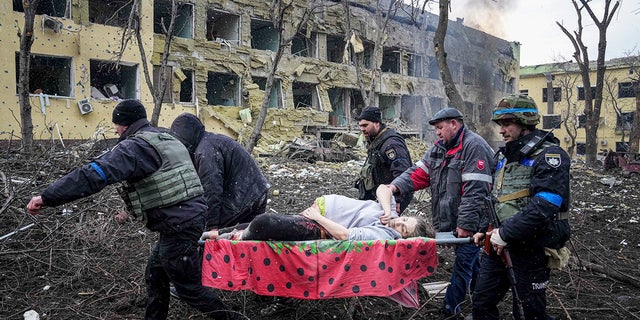 Ukrán mentők és önkéntesek szállítanak egy sérült terhes nőt, akit az ukrajnai mariupoli szülészeti kórház bombázása érintett, 