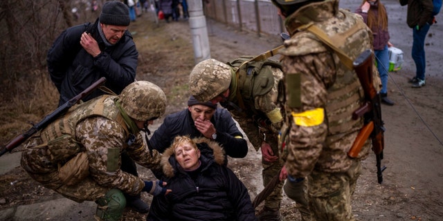 Ukrán katonák vigyáznak egy félájult nőre, miután átkeltek az Irbin folyón, miközben a városból menekültek Kijev (Ukrajna) külvárosában 2022. március 5-én, szombaton. 