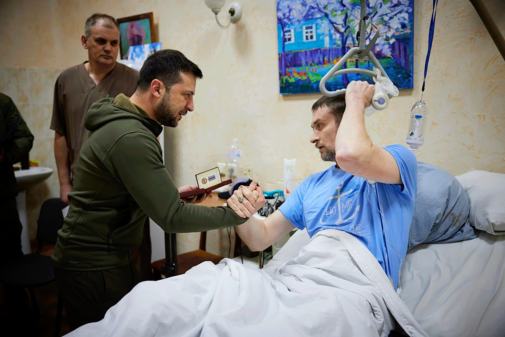 Az Ukrán Elnöki Sajtóiroda által 2022. március 13-án, vasárnap rendelkezésre bocsátott fotón Volodimir Zelenszkij elnök, középen, kezet fog egy sérült katonával, miközben egy kijevi kórházba látogatott.