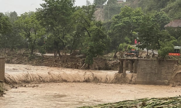Egy autó áll a híd egy szakasza mellett, amelyet az árvíz elmosott az északnyugat-kínai Qingyangban