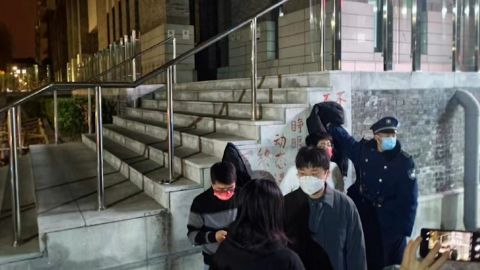 Egy biztonsági őr próbál elfedni a Zero Covid elleni tiltakozó transzparenst a pekingi Pekingi Egyetem campusán.