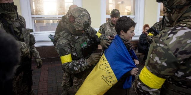 Egy fiú tartja az ukrán nemzeti zászlót, amelyet az ukrán hadsereg tagjai írnak alá 2022. november 19-én az ukrajnai Herszonban.